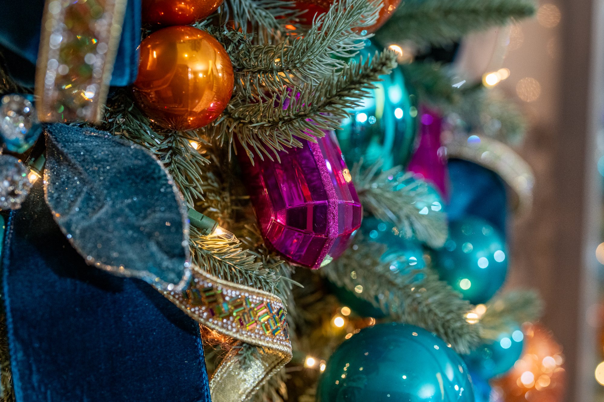 Close-up of a faceted magenta gem ornament among teal glass balls and jeweled ribbon