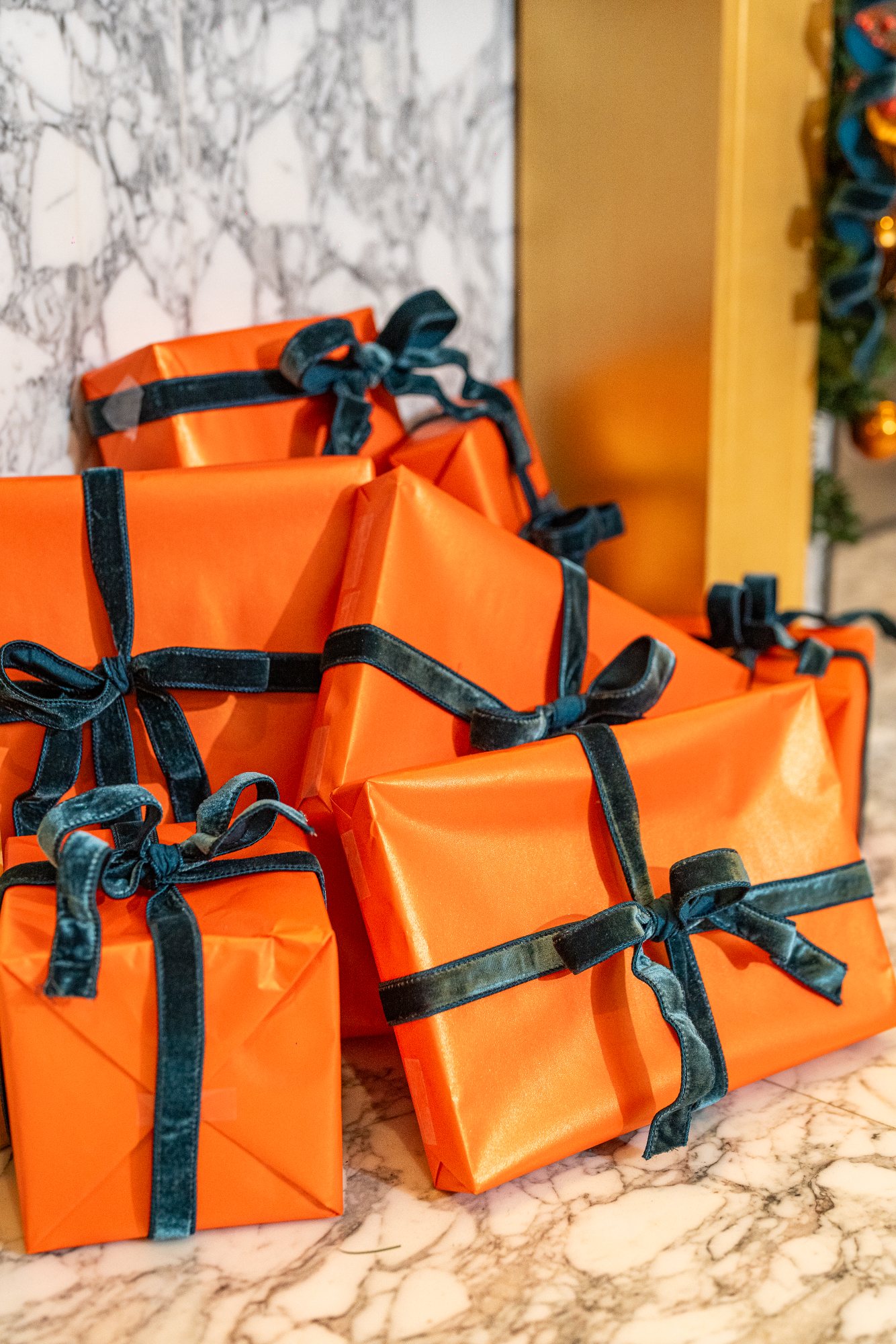 Gifts wrapped in persimmon paper with hand-tied teal velvet ribbon, styled beneath a gilded mantel