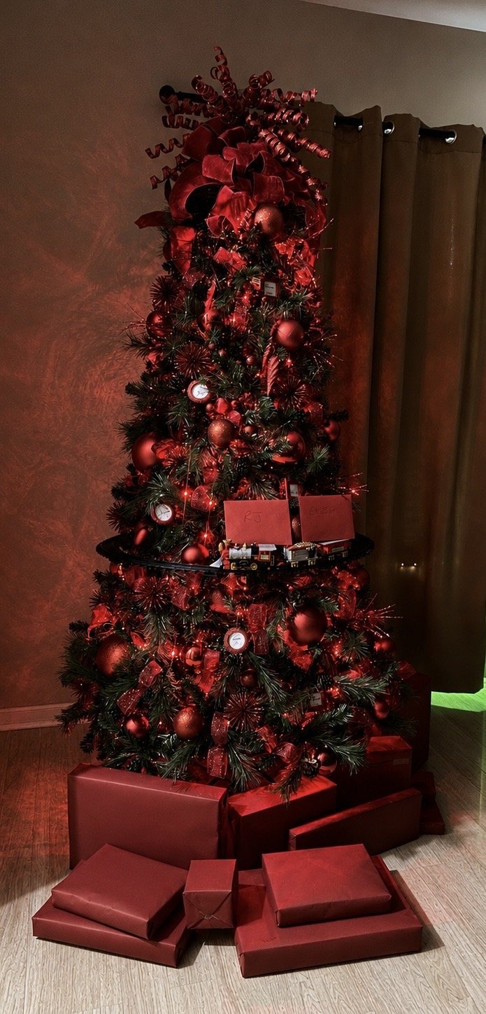 Residential Christmas tree styled in black, white, and silver with velvet ribbon and warm lights beside a curtained window
