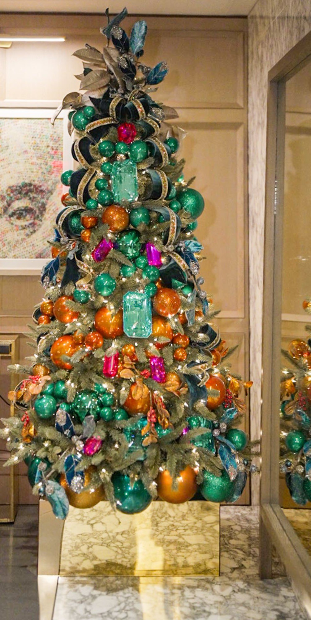 Custom-designed Christmas tree layered with emerald, copper, and fuchsia gem ornaments and teal velvet ribbon